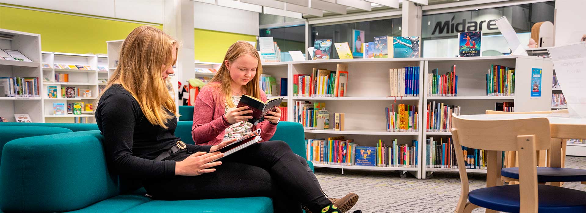 Kaksi nuorta lukee istuu ja lukee kirjaa kirjastossa